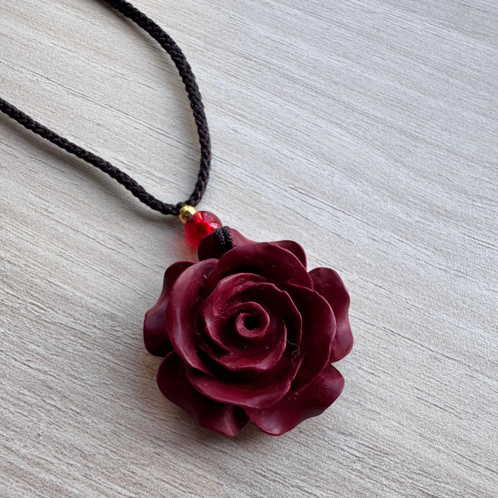Gros plan d’un pendentif en forme de rose bordeaux sculptée à la main sur cordon noir