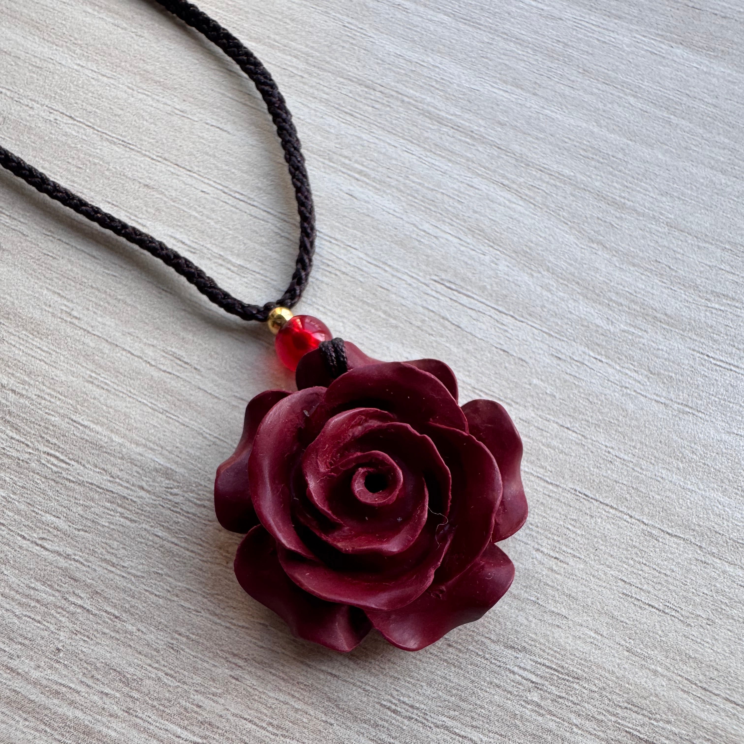 Gros plan d’un pendentif en forme de rose bordeaux sculptée à la main sur cordon noir